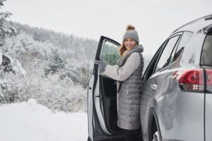 Woman in a grey coat and hat smiling and stepping out of her newly winterized vehicle.