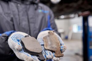 Auto repairman holding two brake pads, one brand new and the other are rusted and worn in an auto repair shop in Springfield, IL.
