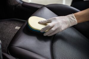 Person with a white rubber glove holding a blue and yellow scrub brush cleaning leather seat upholstery on a vehicle in Springfield, IL