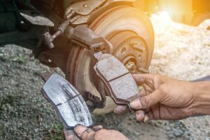 A professional mechanic holding up an old and worm brake pad and a new brake pad to show the difference and when your vehicle needs new brakes.