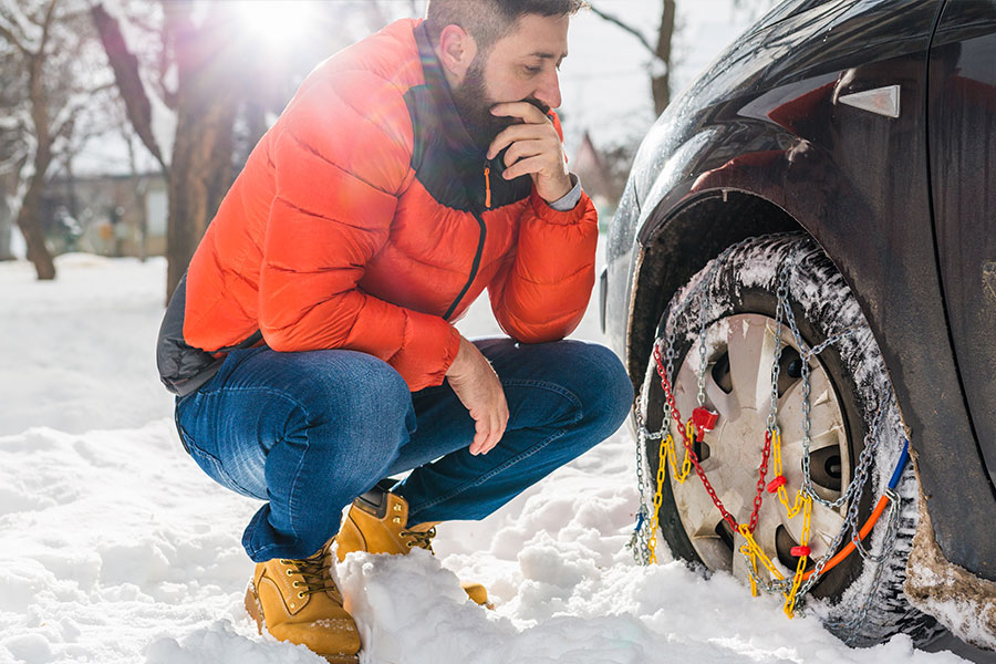 A man in an orange puffer coat puts snow chains on the tires of his vehicle during a snowy winter in Springfield, IL.