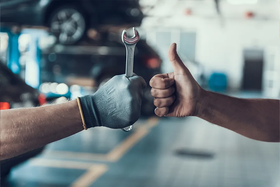 A mechanic’s hand holding a tool and a car owner’s hand giving a thumbs up to indicate a partnership for proper vehicle maintenance in Springfield, IL.